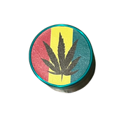 Zielony Grinder Młynek do Tytoniu z Czarnym Liściem Marychy na Tle Rasta