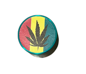 Zielony Grinder Młynek do Tytoniu z Czarnym Liściem Marychy na Tle Rasta